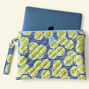 May include: A quilted laptop sleeve with a vibrant lemon slice pattern on a navy and white striped background. The sleeve has a matching wrist strap and a silver zipper. A gray laptop is partially visible inside the sleeve.