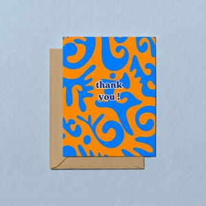 May include: A greeting card with an orange background and blue abstract shapes. The card reads "thank you!" in a white and blue font. The card is inside a brown envelope.