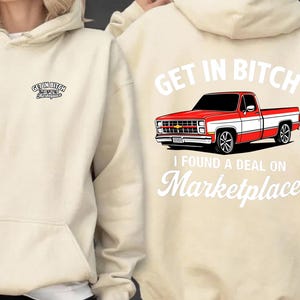 May include: Beige hoodie with a front pocket and drawstring. The front has the text "GET IN BITCH Marketplace". The back shows a red and white pickup truck graphic with "GET IN BITCH" above and "I FOUND A DEAL ON Marketplace" below.