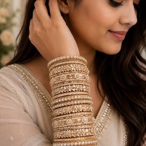 Peut inclure: Un empilement de bracelets joncs dorés ornés de détails métalliques complexes, d'accents en cristal transparent et de bords perlés. L'ensemble se compose de plusieurs bracelets individuels portés ensemble, présentant diverses textures et motifs floraux.
