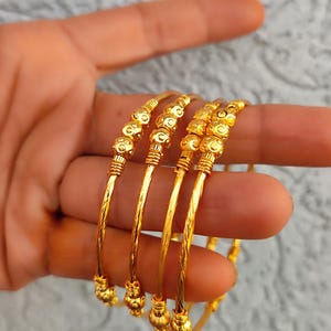 Peut inclure: Un ensemble de quatre bracelets joncs dorés avec une finition polie. Chaque bracelet est conçu avec une tige métallique torsadée et texturée, agrémentée d'une série de petites perles sphériques présentant un détail de surface alvéolé.
