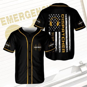 May include: Black baseball jersey with yellow trim and the text "YOUR NAME" on the front. The back features an American flag design with headphones and the word "DISPATCHER". The sleeves have "CHER" and "DISPA" printed on them.