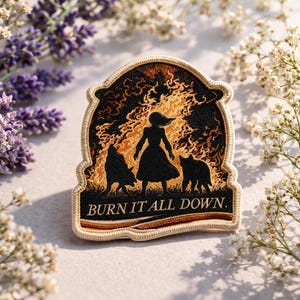 May include: Embroidered patch with a black and gold design featuring a woman and two animals in silhouette against a fiery background. The text "BURN IT ALL DOWN" is at the bottom. The patch has a tan border.