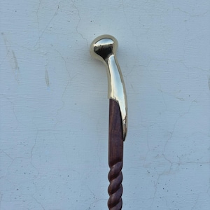 Könnte beinhalten: Ein hölzerner Gehstock mit Messinggriff. Der Griff ist gebogen und hat eine abgerundete Oberseite. Der Schaft ist dunkelbraun und hat ein gedrehtes Seildesign.