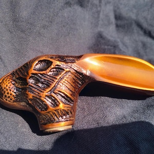 May include: A bronze-colored, carved rabbit head handle. The handle has a textured surface with detailed fur and facial features. The handle is curved and has a smooth, polished finish on the top. The handle is resting on a dark blue fabric.