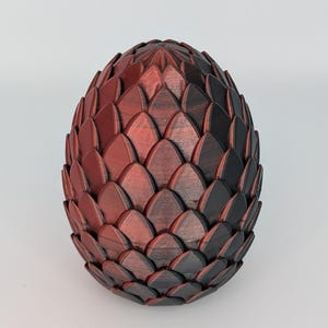 May include: An egg-shaped ornament with a textured, scale-like surface. The scales are in shades of red and black, creating a gradient effect. This decorative item could be a unique piece of art or a display item for a home.