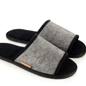 May include: A pair of gray and black open-toe slippers. The slippers have a gray felt upper with a black trim and sole. A small copper-colored accent is visible on the side of one slipper. The background is white.