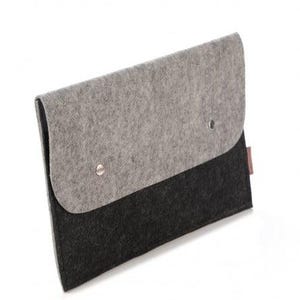 Op de afbeelding: Een grijze en zwarte vilten laptoptas met een klepsluiting. De bovenklep is grijs, vastgezet met twee zilveren klinknagels, en het onderste gedeelte is zwart. Een klein, rechthoekig bruin label is zichtbaar.