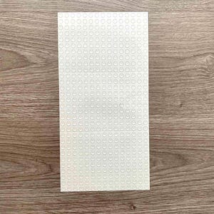 Peut inclure: Une plaque de base rectangulaire blanche pour blocs de construction, avec une grille de petits tenons circulaires en relief. La plaque de base est en plastique et est conçue pour se connecter avec des briques de construction. La plaque de base est posée sur une surface en bois.