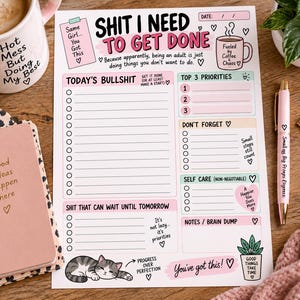Könnte beinhalten: Ein Tagesplaner-Blatt mit der Überschrift "Shit I Need To Get Done" und Abschnitten für Prioritäten, Aufgaben, Selbstfürsorge und Notizen. Die Seite enthält pastellfarbene Akzente in Rosa, Blau und Grün, eine Illustration einer schlafenden Katze sowie Text wie "Progress Over Perfection" und "You've Got This!"