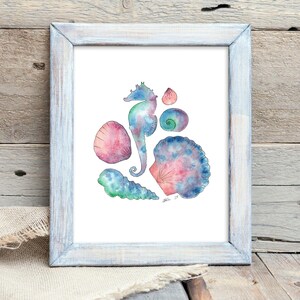 May include: Watercolor print of various seashells and a seahorse in shades of blue, pink, and green. The artwork is framed in a distressed white wooden frame. The image is displayed on a wooden surface with a linen cloth.
