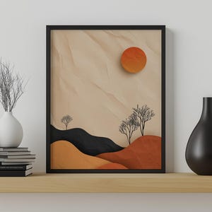 May include: Framed abstract art print featuring a minimalist landscape with rolling hills in black, orange, and tan. An orange sun is in the upper right corner. Two bare trees are in the center. The artwork is displayed on a wooden shelf.