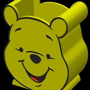 May include: A 3D-rendered yellow Winnie the Pooh head, smiling with a red tongue visible. The design features rounded ears and a boxy base, set against a black background. The cartoon character is a cheerful design.