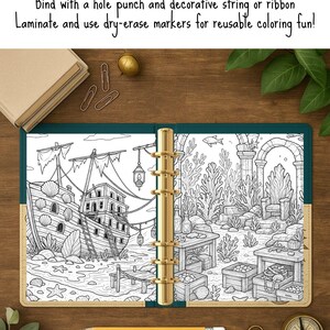 May include: Open, gold-ringed binder with a black and white coloring page featuring an underwater scene with a shipwreck. The binder is open on a wooden surface, with a pencil, paperclips, and a compass nearby. Text on the image encourages the use of dry-erase markers.
