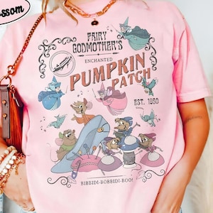 May include: Pink t-shirt with a graphic featuring Cinderella's Fairy Godmother's Enchanted Pumpkin Patch. The design includes Cinderella's glass slipper, mice, and the text "Bibbidi-Bobbidi-Boo!" and "EST. 1950". The shirt has the words "COMFORT COLORS" and "Blossom" on it.