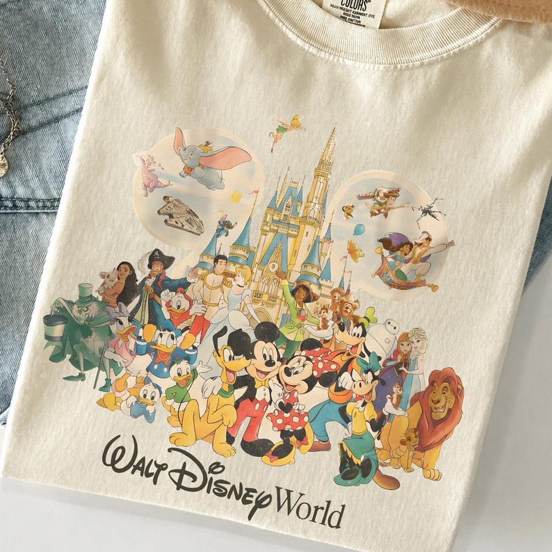 Puede incluir: Una camiseta de color crema con un gran estampado gr&aacute;fico de varios personajes de Disney y un castillo. El dise&ntilde;o incluye a Mickey Mouse, Minnie Mouse, el Pato Donald, Goofy y otros, con el texto Walt Disney World impreso en la parte inferior.