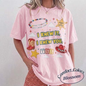 May include: A light pink short-sleeve t-shirt featuring a graphic print with the text "I KNEW IT, I KNEW YOU," a beaded bracelet, a sheriff star badge labeled "INFINITY AND BEYOND," red cowboy boots, a red hat, and blocks spelling "TS5."