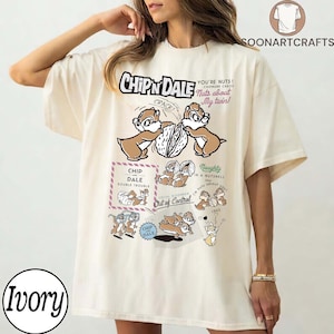 May include: Ivory-colored t-shirt featuring a Chip 'n' Dale graphic. The design includes the text "Chip 'n' Dale", "You're Nuts!", and "Nuts about My twin!" along with cartoon images of the characters. The shirt has a relaxed fit.