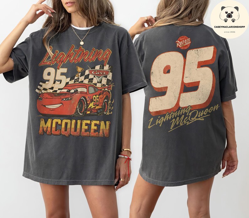 May include: A charcoal gray t-shirt featuring a graphic of the red race car Lightning McQueen with the number 95, a checkered flag, and the text Lightning McQueen on the front, and a large 95 with the text Lightning McQueen on the back.