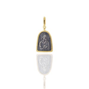 Puede incluir: Colgante dorado con un icono religioso de una madre y un niño. El icono es de color gris oscuro, enmarcado en oro. El colgante tiene un lazo para una cadena y se refleja debajo.