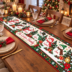 May include: A white fabric table runner featuring a festive Christmas design with green holly borders, red poinsettias, and six illustrated snowmen. Each snowman is labeled with names: Emma, Noah, Olivia, Liam, Sophia, and Ava. The center text reads The Carter Family.