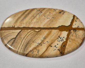 May include: Oval-shaped stone with a polished surface. The stone features a beige and brown colour palette with a cross-like pattern. The design includes dark brown lines and small black speckles, creating a natural, earthy aesthetic.