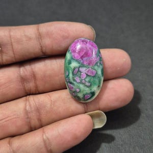Pode incluir: Uma pedra preciosa oval com um padrão rosa e verde marcante. A superfície da pedra apresenta uma mistura de tons rosa e verde, criando um design único. Esta pedra preciosa é ideal para fazer joias ou colecionar.