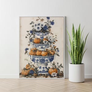 May include: A framed wall art print featuring a three-tiered blue and white porcelain stand filled with orange pumpkins and white and blue flowers. The composition includes additional pumpkins and foliage arranged at the base of the tiered stand.