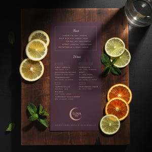 Puede incluir: Una tabla de cortar de madera con un menú de cervezas y vinos, adornada con rodajas de limón, lima y naranja, además de menta. El menú presenta el logotipo "Luna Bar" y el texto "Selections Rotate Seasonally."