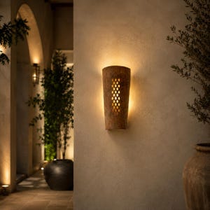 Puede incluir: Un aplique de pared semicilíndrico con un acabado marrón texturizado y desgastado. La lámpara presenta un patrón central vertical recortado con formas de diamante repetidas, permitiendo que la luz cálida se proyecte sobre la pared.