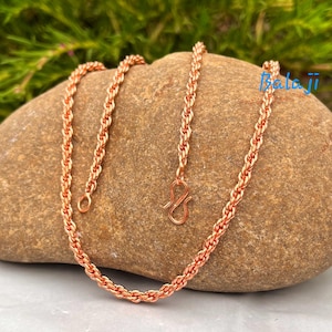 Puede incluir: Un collar de cadena de color cobre con cierre de gancho. El collar se muestra sobre una piedra marrón. La palabra "Balaji" está escrita en azul sobre la piedra.