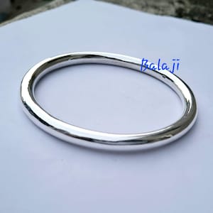 以下が含まれることがあります： 光沢のあるシルバーカラーのバングルブレスレット。ブレスレットは、滑らかで反射性の表面を持つ、ソリッドで丸みを帯びたバンドです。「Balaji」という言葉が青いスクリプトでブレスレットに書かれています。