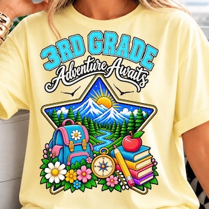 May include: A pale yellow t-shirt featuring a graphic with the text 3RD GRADE Adventure Awaits. The design includes a blue backpack, a stack of books with an apple, a compass, and a mountain landscape with pine trees and a sun inside a star.