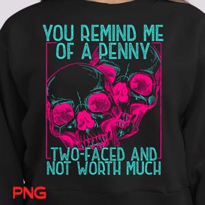 Op de afbeelding: Zwarte sweatshirt met een grafisch ontwerp met twee roze en turquoise schedels. De tekst luidt "YOU REMIND ME OF A PENNY" boven de schedels en "TWO-FACED AND NOT WORTH MUCH" eronder.