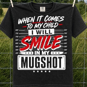 May include: A black short-sleeve t-shirt featuring a white and red graphic of a mugshot height chart. The text reads: WHEN IT COMES TO MY CHILD I WILL SMILE IN MY MUGSHOT. The height markers range from 4'6" to 8'0" in white on both sides.