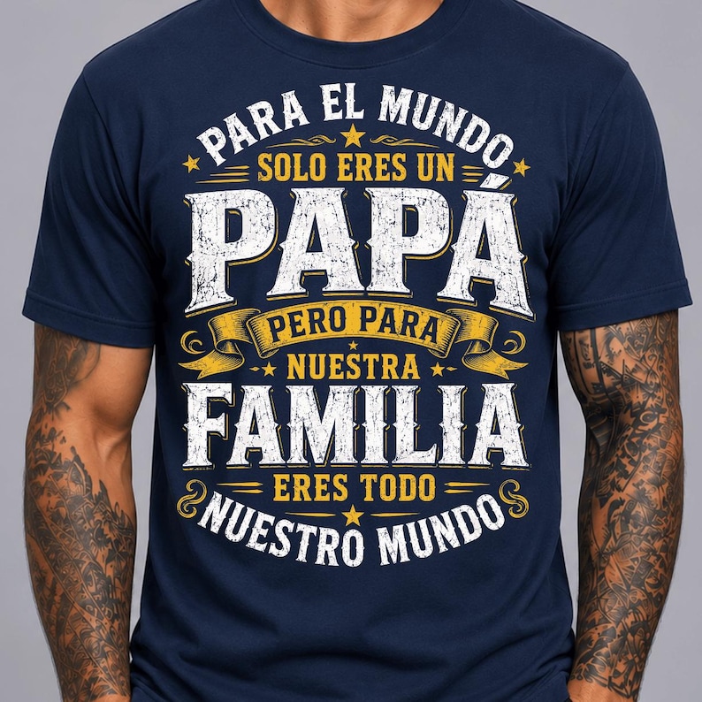 May include: A navy blue short-sleeve t-shirt featuring white and yellow distressed-style text that reads: PARA EL MUNDO SOLO ERES UN PAPA PERO PARA NUESTRA FAMILIA ERES TODO NUESTRO MUNDO, accented with small yellow stars and decorative banners.
