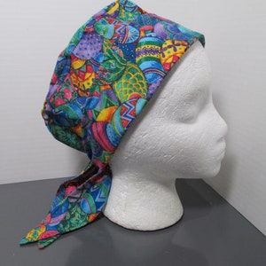 May include: A colorful Easter-themed head covering with a vibrant pattern of decorated eggs in shades of blue, green, yellow, pink, and purple. The fabric is tied at the back, and the head covering is displayed on a white mannequin head.