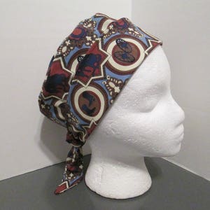 May include: A blue, brown, and white patterned fabric headband with a tie at the back. The headband is worn on a white mannequin head.