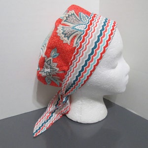 May include: A red and white patterned surgical cap with a blue and gray wavy trim. The cap is tied at the back with a long tail.