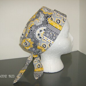 May include: A gray and yellow patterned fabric scrub hat with a tie. The hat is on a white styrofoam head.