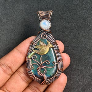 Peut inclure: Pendentif artisanal avec une pierre de labradorite en forme de goutte d'eau, un oiseau en laiton et un fil métallique. Le pendentif a un accent de pierre de lune et mesure environ 5 cm de long.