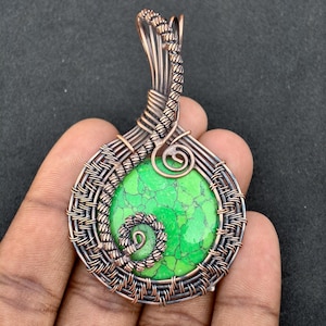 May include: A handcrafted pendant featuring a vibrant green stone, intricately wrapped with copper wire. The wirework forms a circular frame around the stone, with decorative spirals. The pendant is designed to be worn as jewelry.