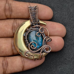 Peut inclure: Pendentif artisanal avec un croissant de lune en laiton, un travail de fil de cuivre complexe et une pierre précieuse bleue ovale au centre. Le pendentif a un design artistique unique avec une bélière pour une chaîne.