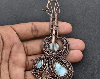 May include: A copper wire-wrapped pendant in the shape of a guitar. The pendant features two light blue, teardrop-shaped stones and a round stone. The guitar's body and neck are intricately woven with copper wire.