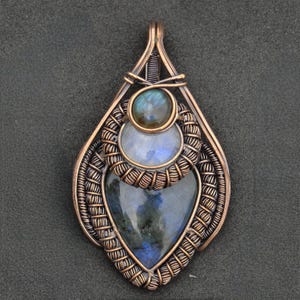 Peut inclure: Pendentif en cuivre fait &agrave; la main avec trois pierres pr&eacute;cieuses incrust&eacute;es. La pierre sup&eacute;rieure est une petite pierre ronde bleu-vert iris&eacute;e. En dessous, une pierre ronde bleu clair et en bas, une pierre bleue fonc&eacute;e en forme de c&oelig;ur.
