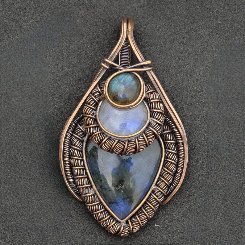 Peut inclure: Pendentif en cuivre fait &agrave; la main avec trois pierres pr&eacute;cieuses incrust&eacute;es. La pierre sup&eacute;rieure est une petite pierre ronde bleu-vert iris&eacute;e. En dessous, une pierre ronde bleu clair et en bas, une pierre bleue fonc&eacute;e en forme de c&oelig;ur.
