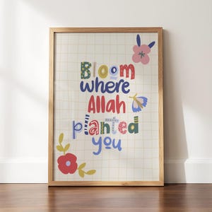 May include: A framed wall art print featuring a light grid background with the text Bloom where Allah planted you in colorful, patterned letters. The design includes a pink flower, a blue butterfly, and a red flower with yellow leaves.