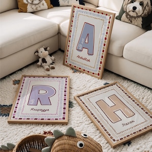 May include: Three rectangular framed wall art prints featuring large letters A, R, and H in light blue, lavender, and beige. Each print includes a decorative border, a name in English script, and corresponding Arabic text inside the letter.