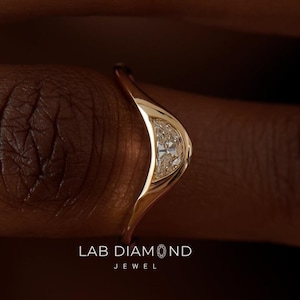 Könnte beinhalten: Ein goldfarbener Ring mit geschwungenem Design, besetzt mit einer Ansammlung kleiner, klarer Steine. Der Ring befindet sich an einem Finger, mit dem Text "LAB DIAMOND JEWEL" sichtbar. Das Design des Rings ist modern und elegant.