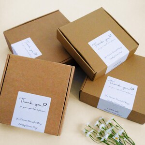 May include: Three square brown cardboard shipping boxes with white labels. Each label features the text Thank you for your support and patience, You Deserve Beautiful Things, Sending Warm Hugs, and OPEN ME Have a nice day, with a small heart icon.